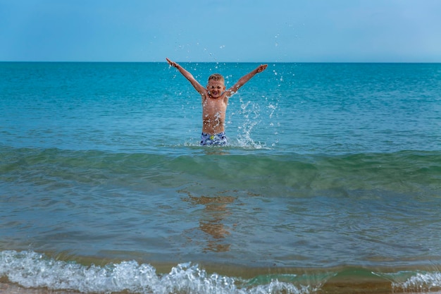 Een jongen zwemt op een zonnige dag in de zee. Het kind verheugt zich en spettert in het water