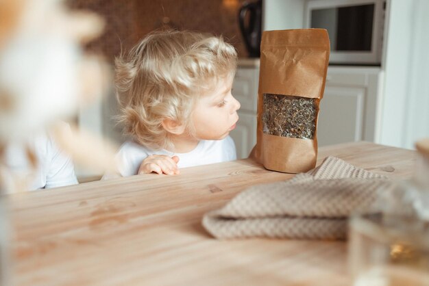 Een jongetje zit aan de keukentafel en kijkt naar een zakje losse thee