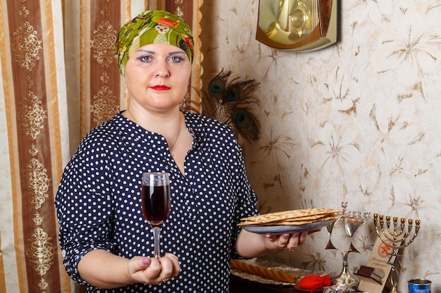 Een joodse vrouw in een kisui rosh-hoofdtooi met een glas wijn en matza in haar handen