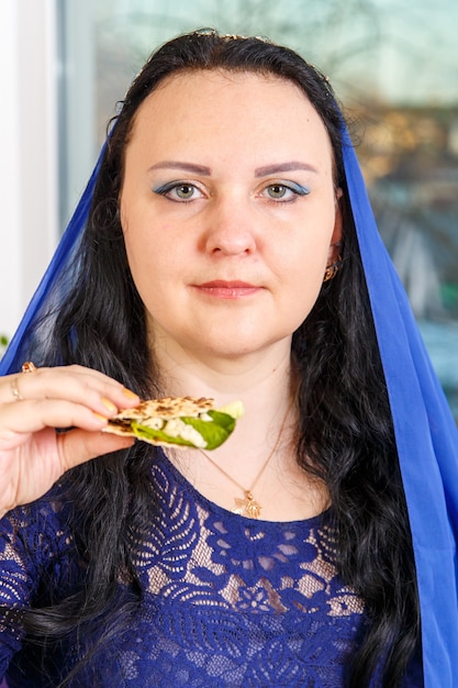 Een joodse vrouw met haar hoofd bedekt met een blauwe cape aan de Pesach Seder-tafel eet moror hazeret matzah. Verticale foto