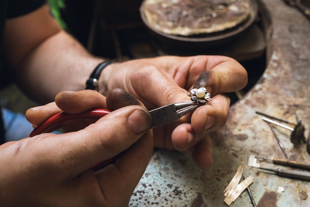 Een juwelier demonteert een gouden ring met parels in een werkplaats, close-up