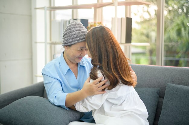 Een kankerpatiënt vrouw met hoofddoek knuffelen haar ondersteunende dochter binnenshuis, gezondheid en verzekering concept.