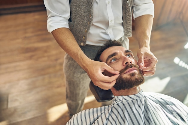 een kapper die de snor van zijn klant met beide handen aanraakt tijdens het aanbrengen van haarproduct