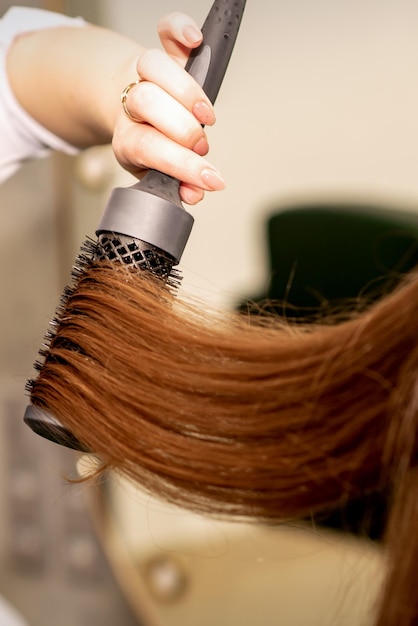 Een kapper droogt lang bruin haar met een haardroger en ronde borstel in een schoonheidssalon