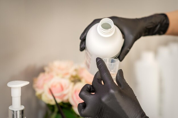 Een kapper in zwarte handschoenen bereidt haarverf met een fles in een kapsalon, close-up.