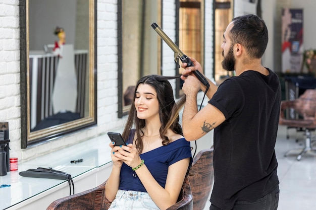 Een kapper vormt het haar van zijn klanten en de klant speelt aan de telefoon Foto van hoge kwaliteit