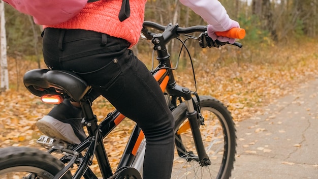 Een kaukasisch kind rijdt fietsweg in het herfstpark Klein meisje rijdt op een zwarte oranje fiets in het bos Kid gaat fietssporten Biker motion ride met rugzak en helm Mountainbike hardtail