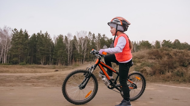 Een kaukasisch kind rijdt op een fietspad in een vuilpark, een meisje dat een zwarte oranje fiets berijdt in racetrac