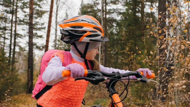 Een kaukasische kinderen lopen met de fiets in het herfstpark, een klein meisje dat een zwarte oranje fiets in de bossen loopt