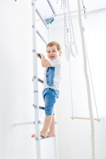 een kind aan de Zweedse muur sport thuis een jongen beklimt een ladder met een touw het concept van sport en gezondheid