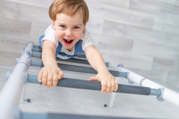 Een kind aan de Zweedse muur sport thuis, een jongen klimt met een touw op een ladder, het concept van sport en gezondheid