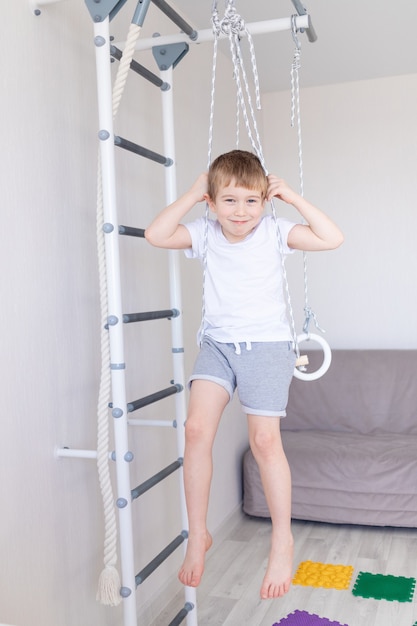 Een kind aan de Zweedse muur sport thuis, een jongen klimt met een touw op een ladder, het concept van sport en gezondheid