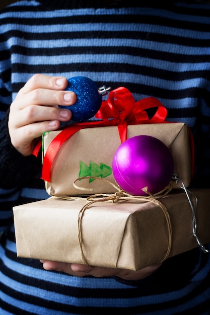 Een kind dat een kerstcadeau geeft met een rood lint en decoratieve ballen