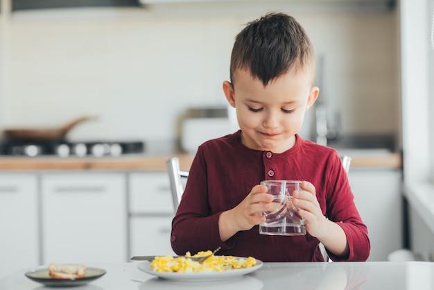 Een kind drinkt 's middags in een witte lichte keuken water uit een glas