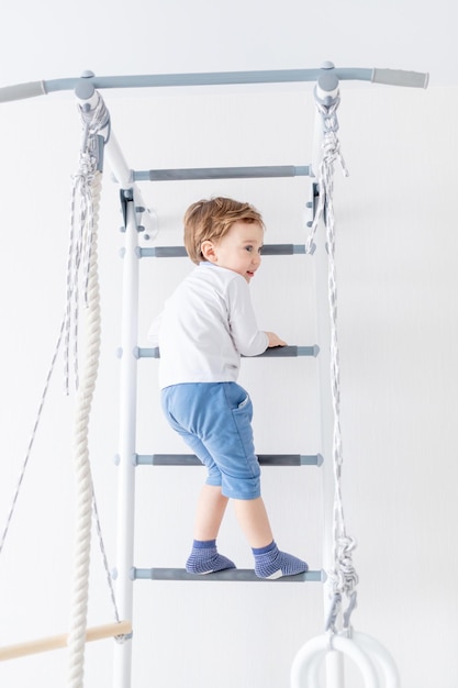 een kind een jongen sport of doet oefeningen op de Zweedse muur van het huis
