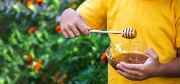 Een kind eet honing in de tuin uit een doorzichtige kom natuur