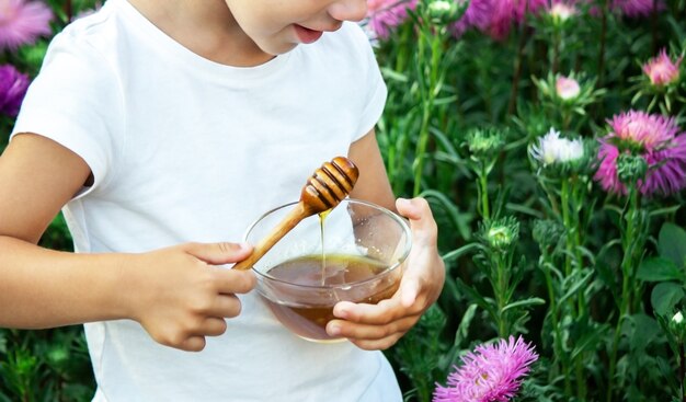 Een kind eet honing in een bloementuin. Selectieve focus