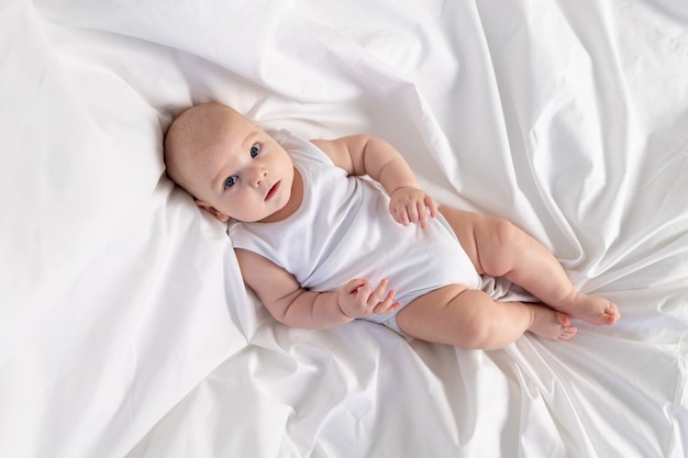 Een kind in de ochtend op een wit bed. Textiel en beddengoed voor kinderen. Een pasgeboren baby is wakker geworden of gaat naar bed