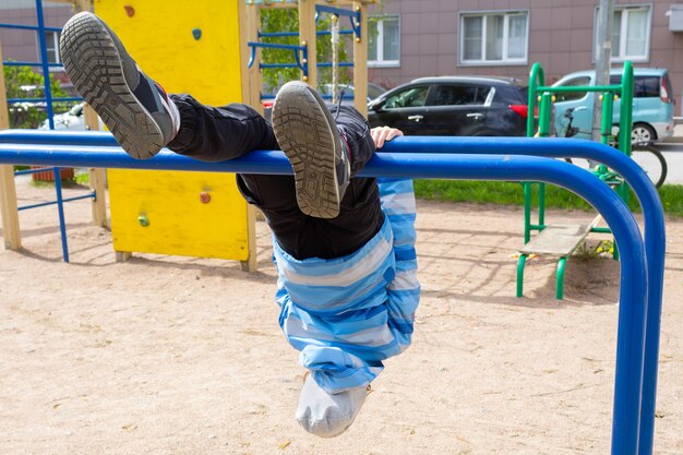 Een kind in de speeltuin hangt ondersteboven aan de tralies. Zolen van sneakers op de voorgrond.