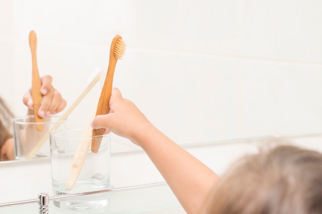 Een kind in een badkamer steekt een bamboetandenborstel in een glas. geen afvalconcept.