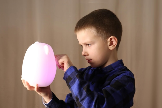 een kind in een blauw shirt houdt een lamp vast in de vorm van een witte haas gloeit