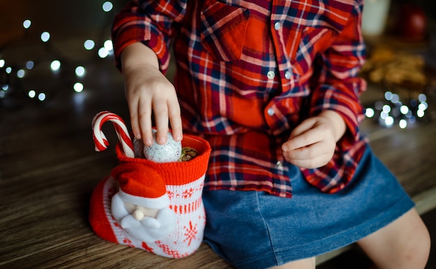 Een kind in een geruit rood shirt neemt snoep van een zoet kerstcadeau