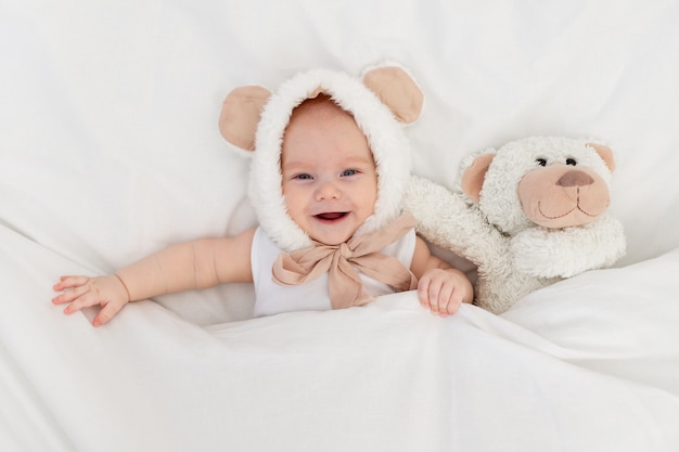 Een kind in een grappige hoed met oren met een teddybeer onder de deken. Textiel en beddengoed voor kinderen. Een pasgeboren baby is wakker geworden of gaat naar bed