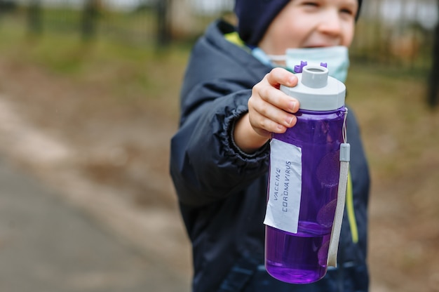 Een kind in een medisch masker houdt een fles