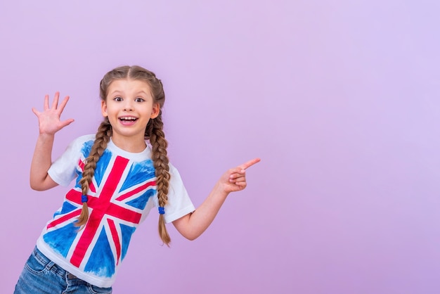 Een kind in een overhemd met een britse vlag wijst naar uw advertentie op een afgelegen roze achtergrond.