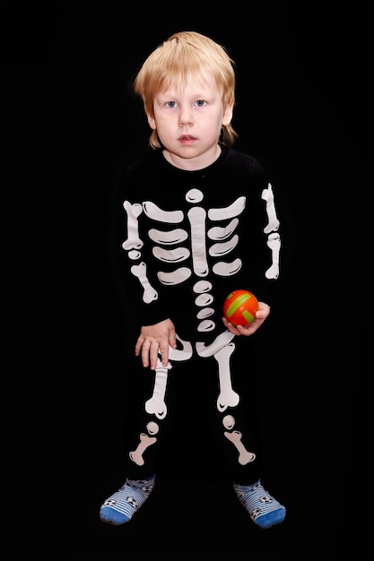 Een kind in een skeletkostuum met een oranje bal in zijn hand zwarte achtergrond