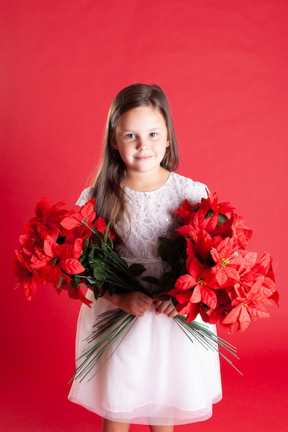 Een kind in een witte jurk houdt twee boeketten kerstbloemen vast