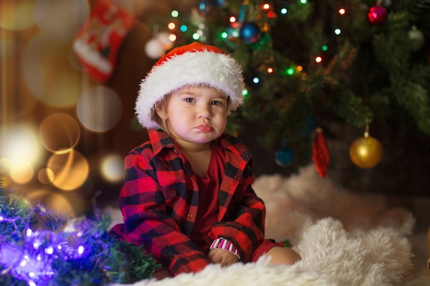 Een kind in rode kleren zit te wachten op het nieuwe jaar. het concept van het vieren van Kerstmis om middernacht. vakantie kostuum