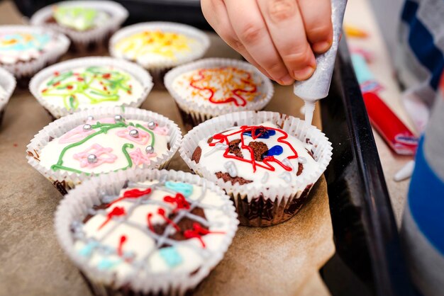 Foto een kind knijpt gekleurde glazuur uit een buis op chocolade bruine cupcakes bedekte decoraties