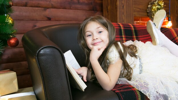 Een kind leest een interessant boek bij de kerstboom.