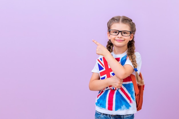 Een kind met een bril en een T-shirt met een Britse vlag houdt Engelse boeken in zijn hand op een roze geïsoleerde achtergrond.