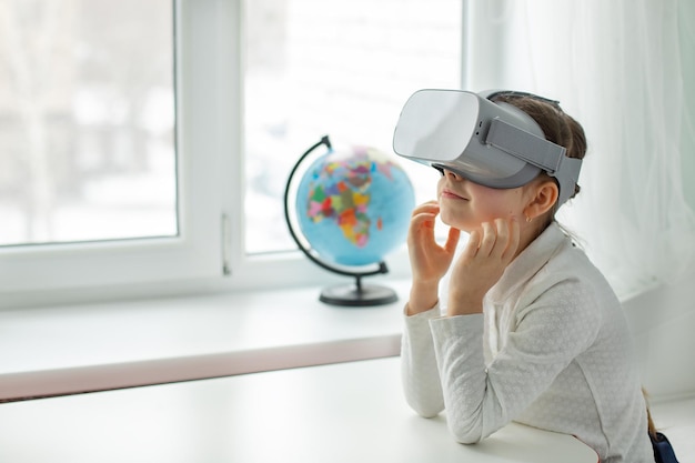 Een kind met een virtual reality-headset zit thuis binnenshuis aan tafel Een meisje verkent de wereld van virtual reality via video en games