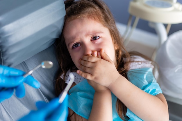 Een kind met haar handen voor de mond kijkt naar het gereedschap van een tandarts