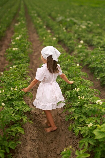 Een kind op blote voeten in een jurk spint tussen rijen aardappelen in het bloeiseizoen