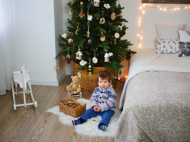 Een kind op de vloer bij de kerstboom en nieuwjaarsversieringen