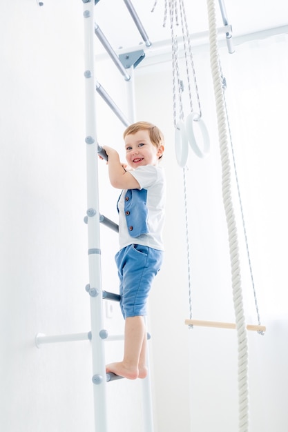 Een kind op de Zweedse muur sport thuis, een jongen beklimt een ladder met een touw, het concept van sport en gezondheid.