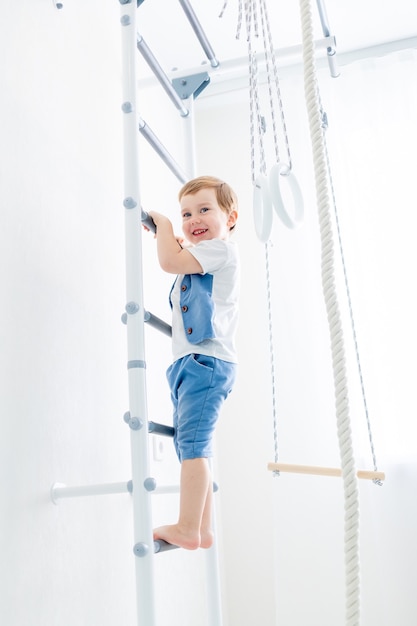 Een kind op de zweedse muur sport thuis, een jongen beklimt een ladder met een touw, het concept van sport en gezondheid.