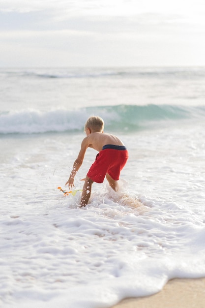 Een kind op het strand speelt in de golven van de oceaan. Jongen op de oceaan, gelukkige jeugd. tropisch leven.