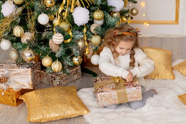 Een kind pakt thuis een nieuwjaarscadeau uit bij een kerstboom met een gouden decor