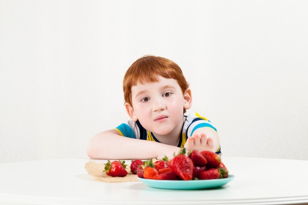 Een kind reikt naar aardbeien aan de overkant van de tafel om zoete bessen te eten
