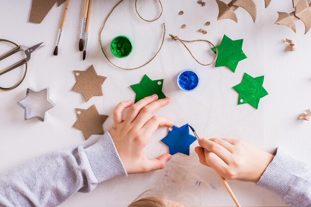 Een kind schildert een gouache-ster van karton voor doe-het-zelf kerstversieringen bovenaanzicht