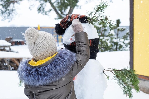 Een kind schildert het gezicht van een sneeuwpop met verf winterentertainment en creativiteit die een sneeuwpop beeldhouwt in de winter buiten