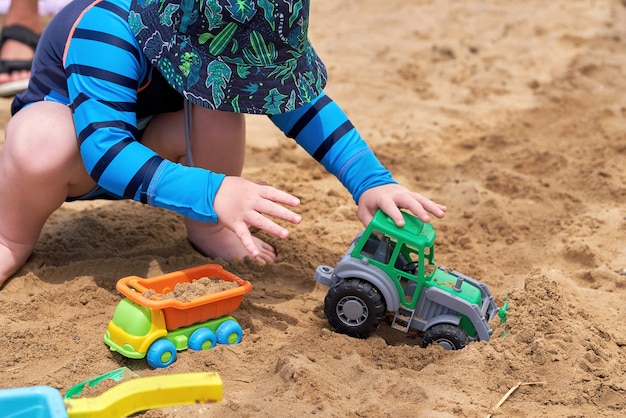 Een kind speelt in een speelgoedauto op een zandstrand op een zonnige zomerdag