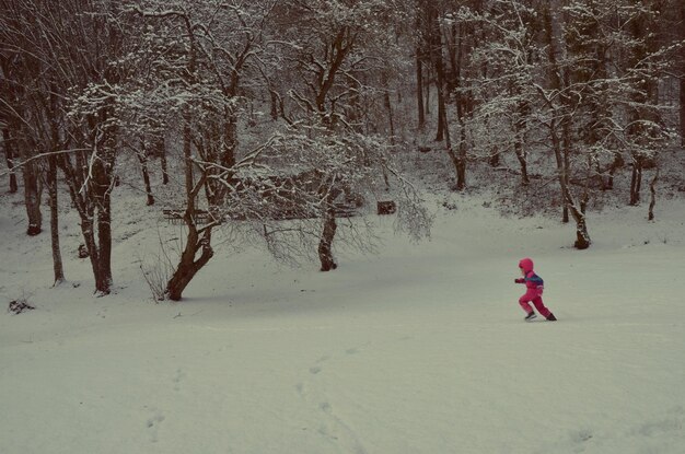 Een kind speelt op een met sneeuw bedekt veld bij kale bomen.