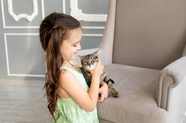 Een kind speelt thuis met een kat, een klein meisje houdt een kat in haar armen, het concept van de vriendschap van een kind met dieren