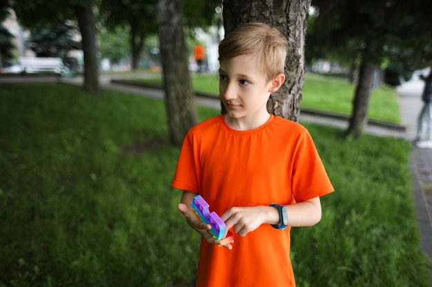 Een kind staat in een park met zijn rug tegen een boom met een anti-stress siliconen speelgoed in zijn handen